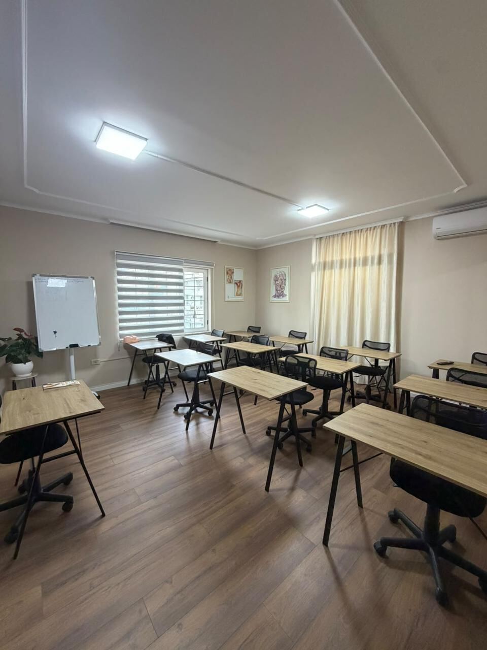 The theory classroom with twelve desks, task chairs, a whiteboard and anatomy prints on the wall.